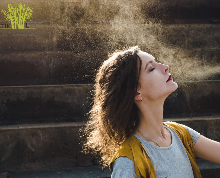 Young woman spraying face with thermal water. Enjoying, skin care concept.